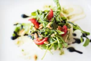 a green salad with pine nut, vinegar and tomatoes sprinkled on top