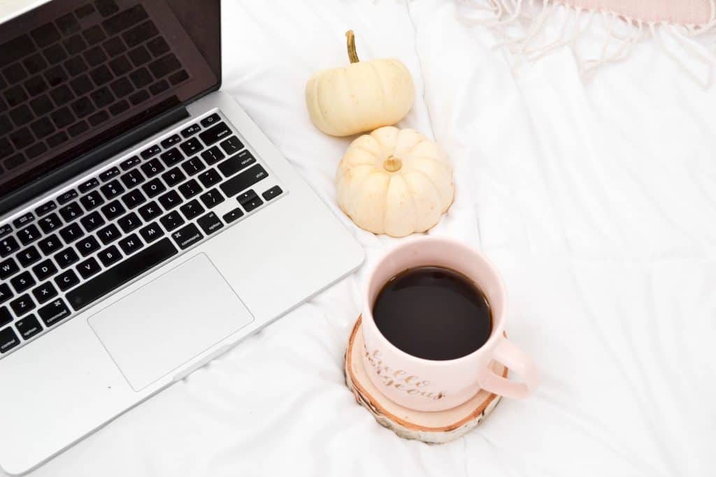 Image of a cup of coffee next to a laptop and two white mini pumpkins