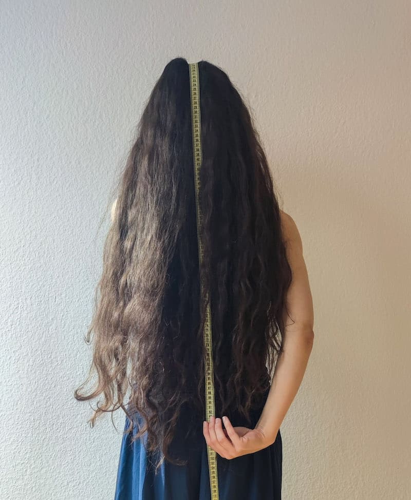 Person with long hair having a measuring tape hanging down the middle of the hair mass